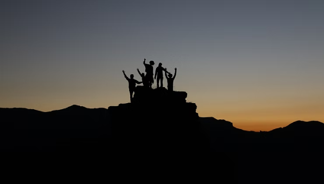 photo d'un groupe de personne en haut d'une montagne au coucher du soleil